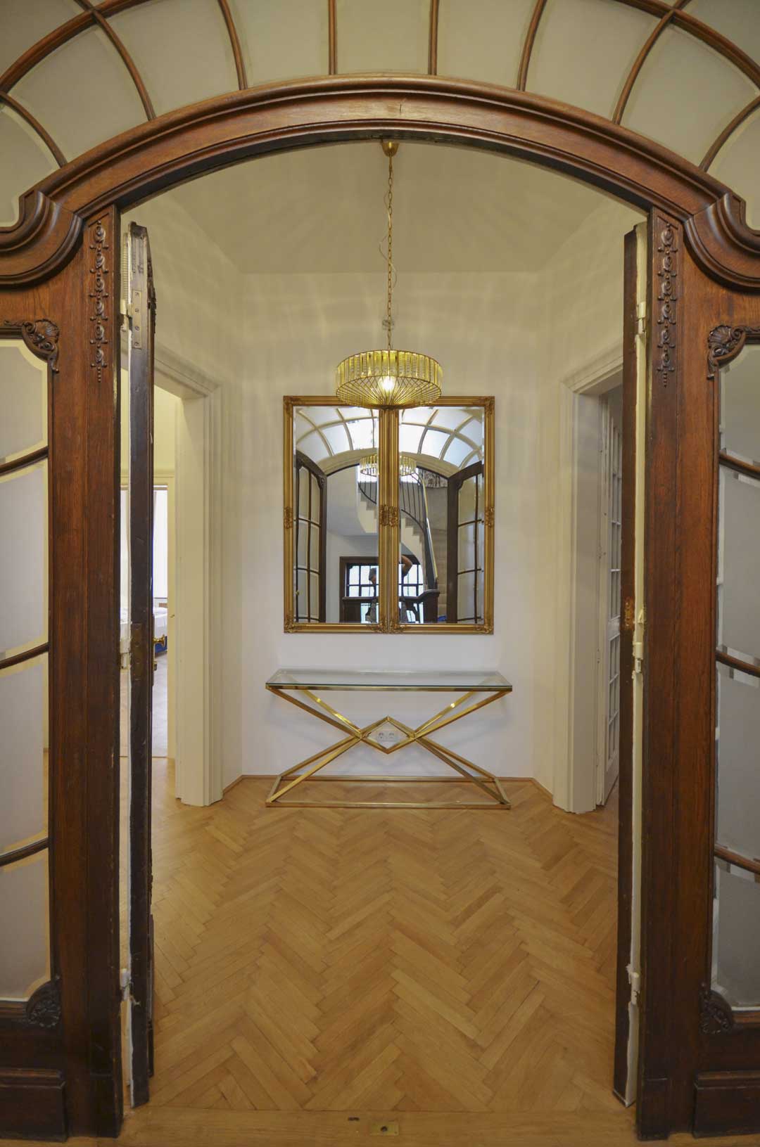 Beautiful historic entrance with a gold entrance table and a big mirror, on the side wooden doors
